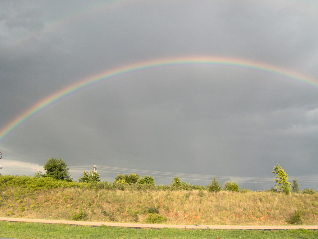 Arcobaleno in cielo grigio sopra terreno erboso