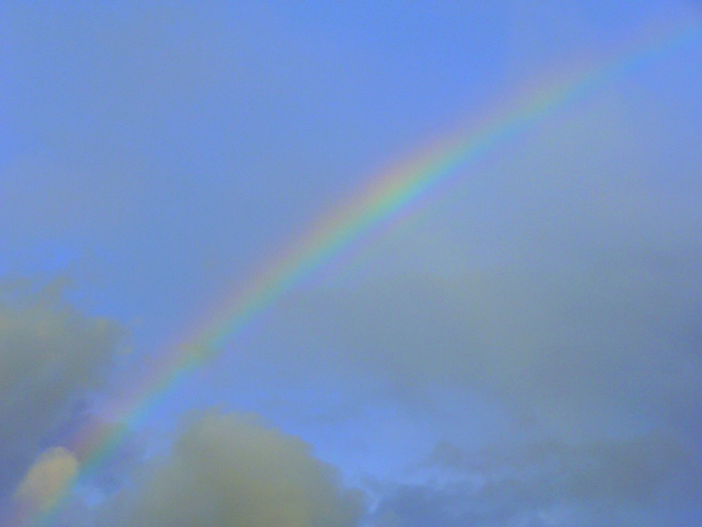 Arcobaleno in diagonale in bel cielo azzurro con poche nuvole