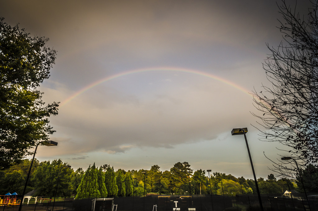 Arcobaleno sottile sopra bosco vicino a città