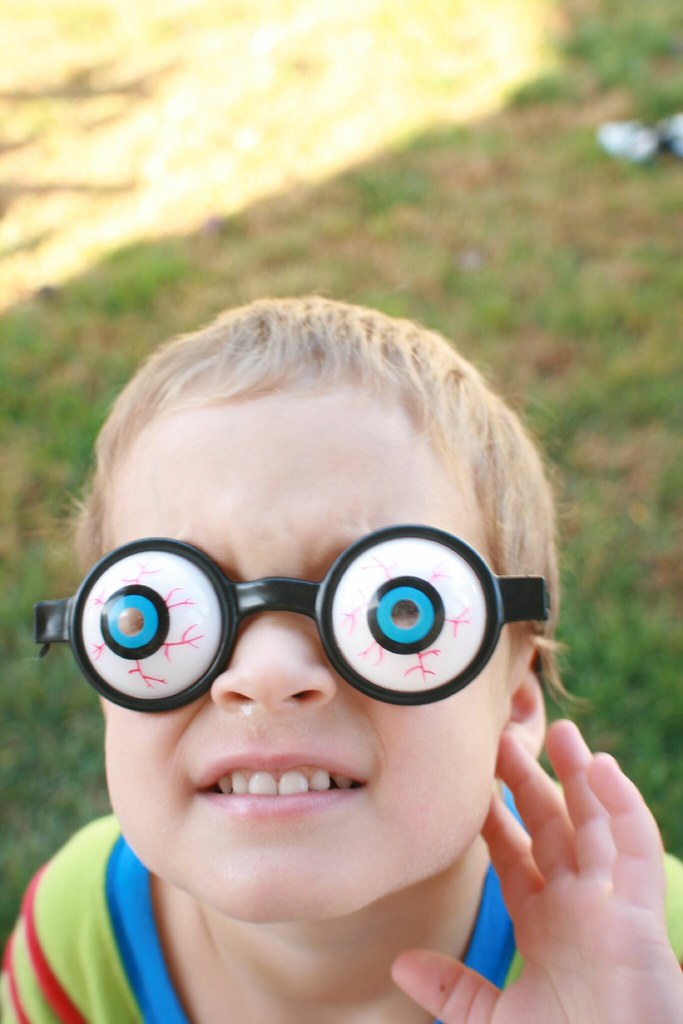 Bambino sul prato che indossa occhiali a forma di occhi