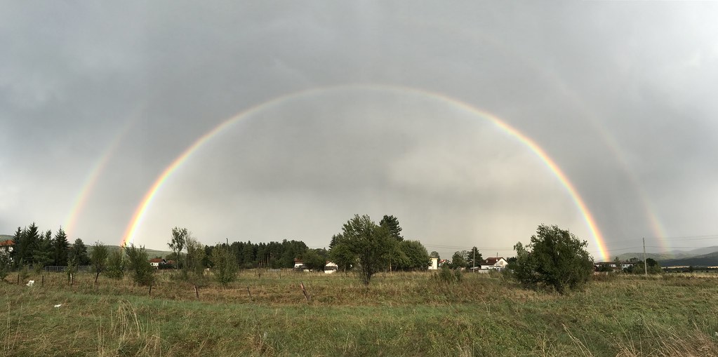 Doppio arcobaleno fantastico molto luminoso in cielo plumbeo