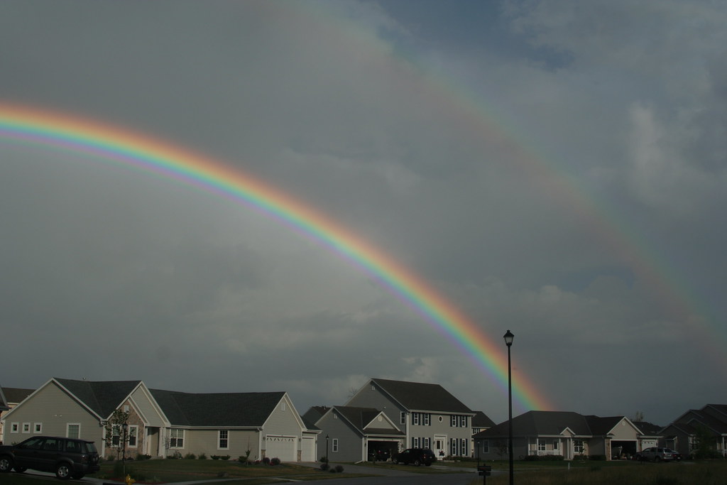 Doppio arcobaleno in cielo plumbleo sopra diverse villette