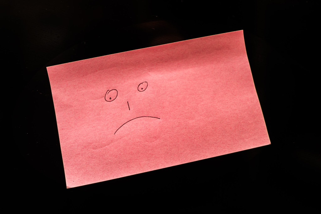 Faccina triste disegnata su foglio rosa con sfondo nero