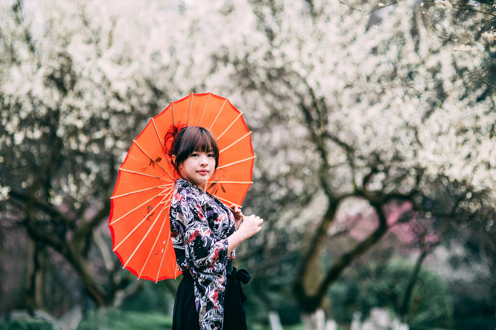 Graziosa ragazza giapponese con ombrello arancione davanti a alberi