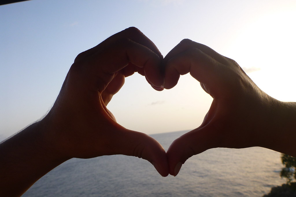 Mani unite a cuore verso il mare e il cielo