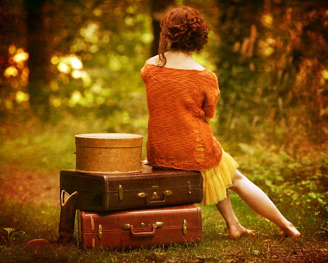 Ragazza di spalle seduta su valigie nel bosco con stupenda atmosfera vintage