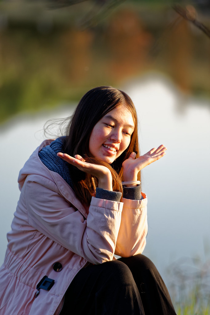 Ragazza sorridente seduta vicino al lago con mani aperte sotto il viso