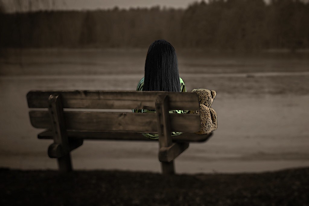 Ragazzina sola seduta su panchina di fronte al lago