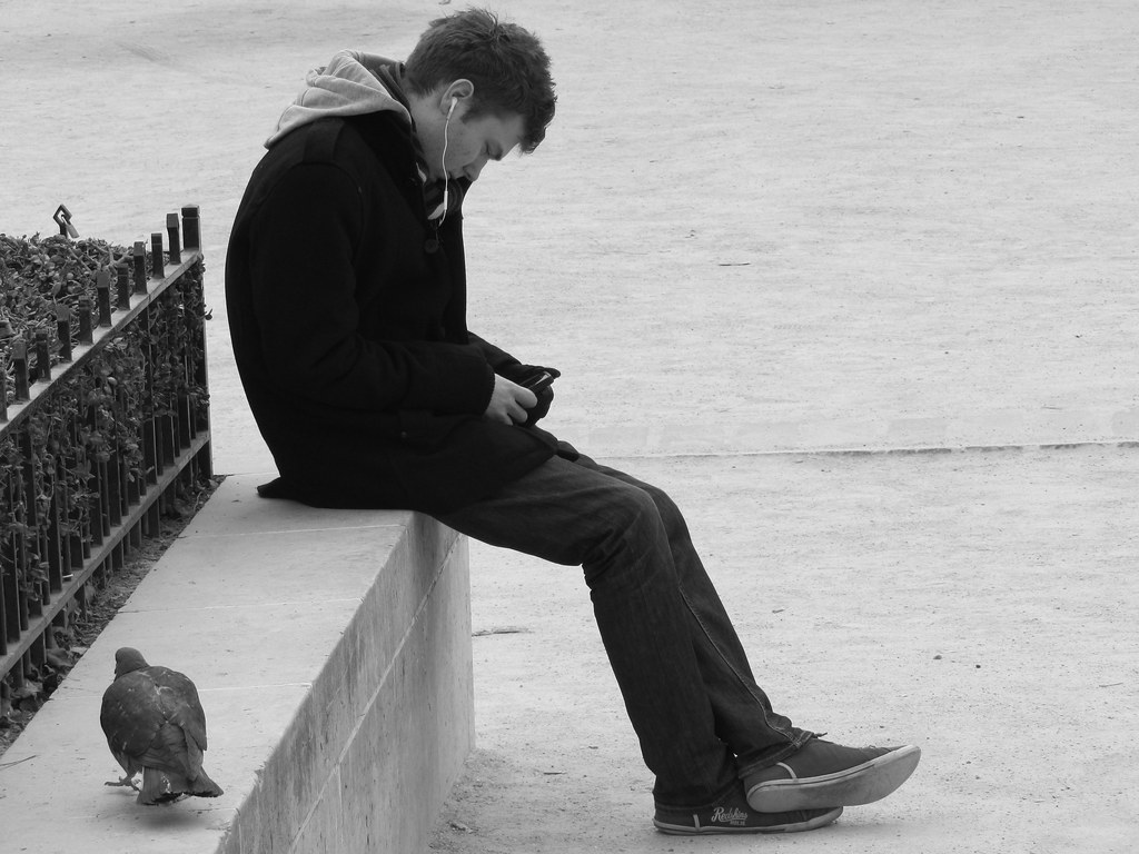 Ragazzo seduto in strada vicino a piccione a Parigi che ascolta musica
