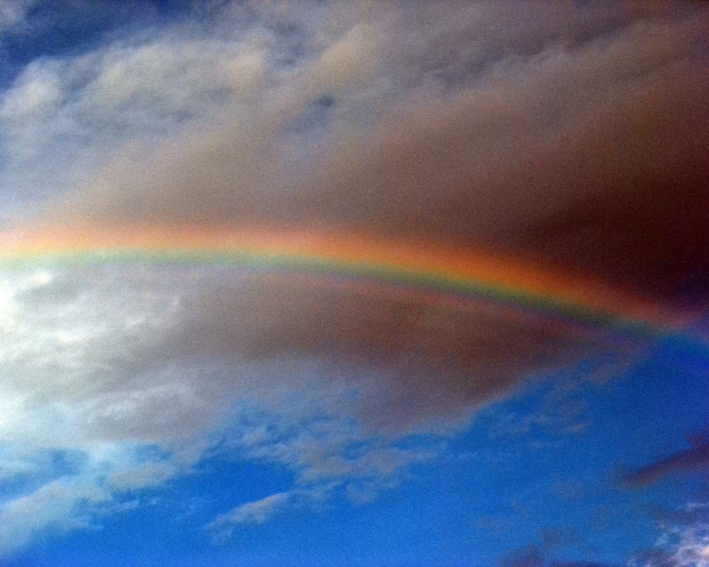 Tratto di arcobaleno in cielo azzurro con brutta nuvola