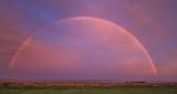 Arcobaleno come arco perfetto in paesaggio violaceo