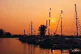 Barche su mare arancione che riflette luce del tramonto