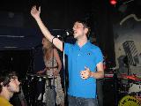 Immagine cantante Cantante con maglietta azzurra e mano alzata vicino a ragazza che suona