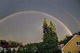 Doppio arcobaleno sopra alberi irti e tetti di case