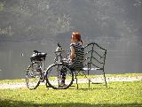 Ragazza con capelli rossi seduta al lago vicino a bicicletta