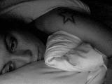 Immagine triste Ragazza triste con tatuaggio sulla spalla al letto in bianco e nero