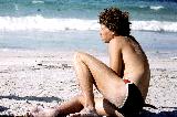 Ragazzo riccio in costume su spiaggia con bella sabbia bianca